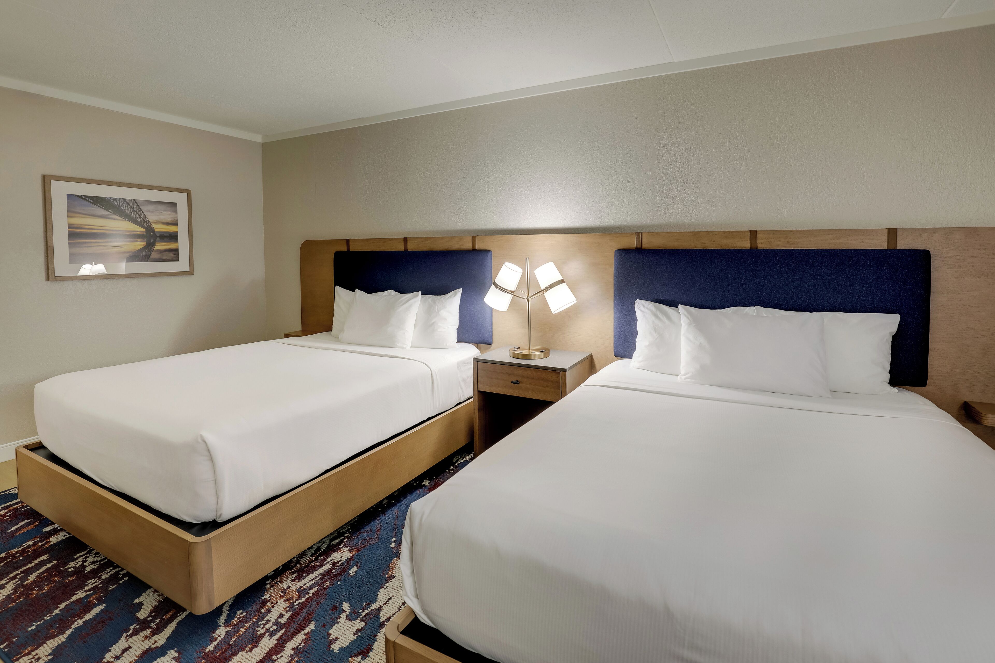 A hotel room with two single beds, a nightstand with a lamp, and a framed picture on the wall.