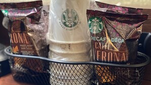 Een etalage van een koffie winkel met een witte beker, twee Starbucks zakken en een gemarkeerde koffiemolen.