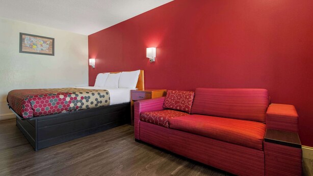 A hotel room with a bed, a red sofa, and two wall-mounted lights. - Econo Lodge Goldsboro Hwy 70 (Goldsboro)