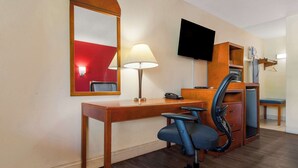 A hotel room with a wooden desk, a chair, a television mounted on the wall, a mirror, a lamp, and a small seating area with a chair and a table. - Econo Lodge Goldsboro Hwy 70 (Goldsboro)