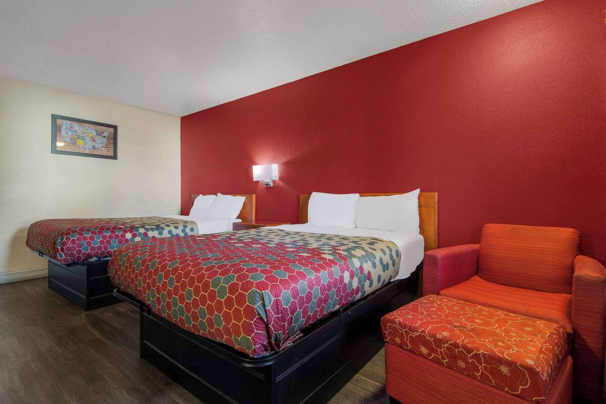 Ein Hotelzimmer mit zwei Betten, einer roten Wand, einem Nachttisch und einem roten Sessel.