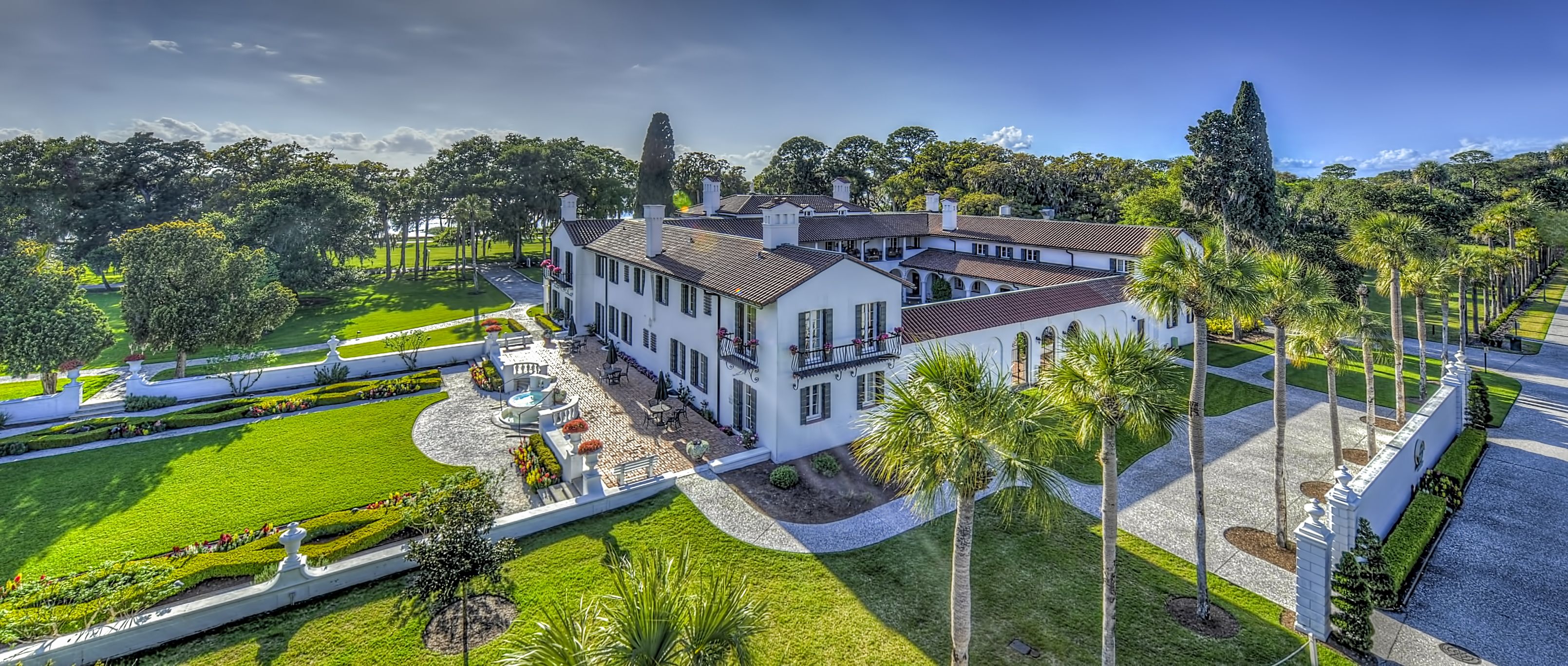 A large, white, multi-story building with a symmetrical facade, surrounded by well-manicured gardens and palm trees.