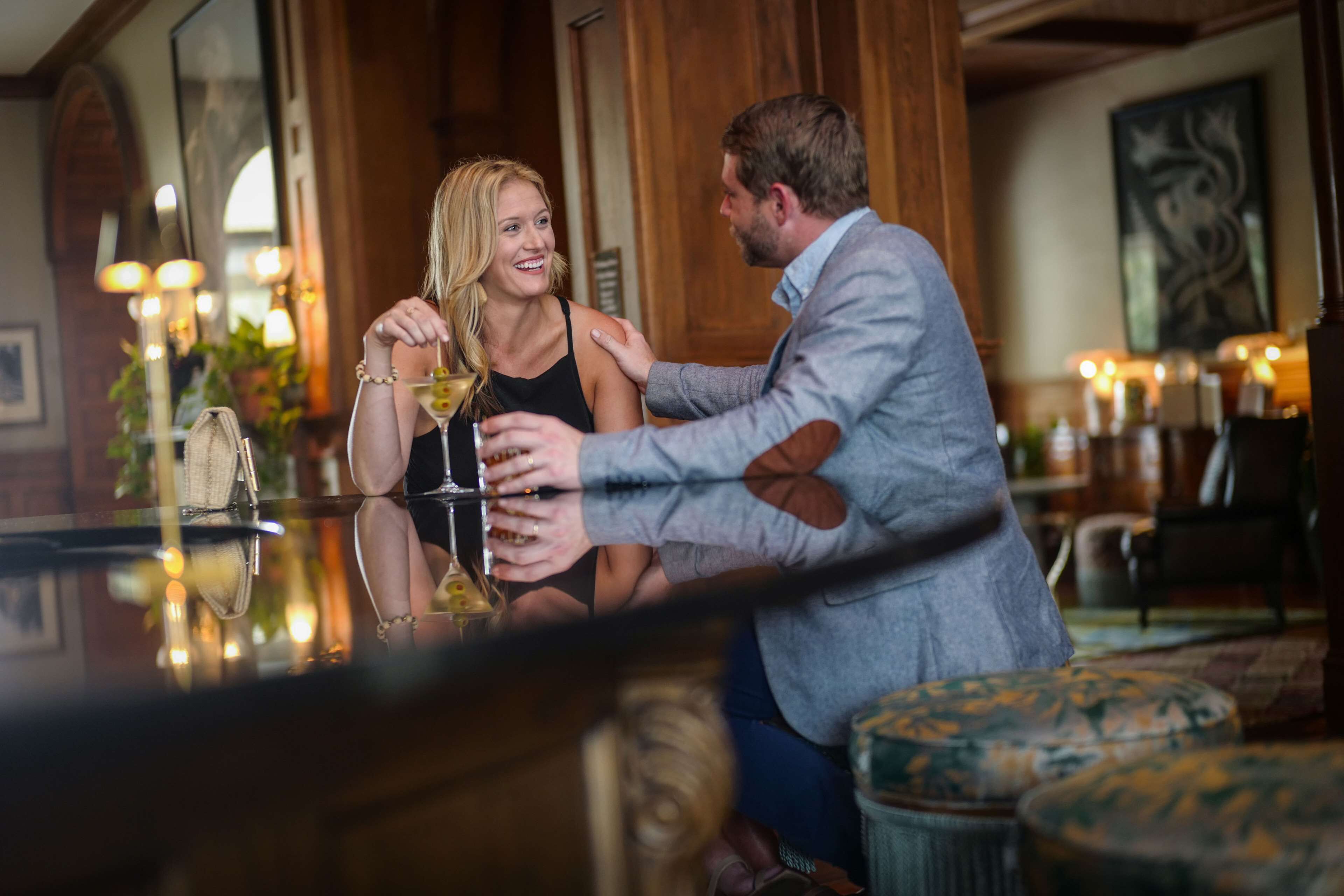 Una pareja sentada en un bar, cada uno con una copa de vino, en un ambiente cálido con decoración de madera y un candelabro.
