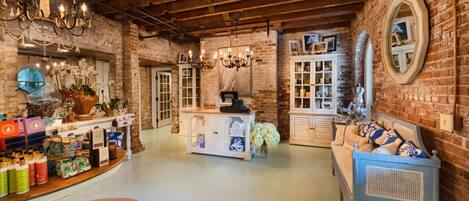 Ambiente rustico con pareti in mattoni a vista, soffitto in legno e un lampadario. Presente una reception con bancone bianco e un divano con cuscini decorati.