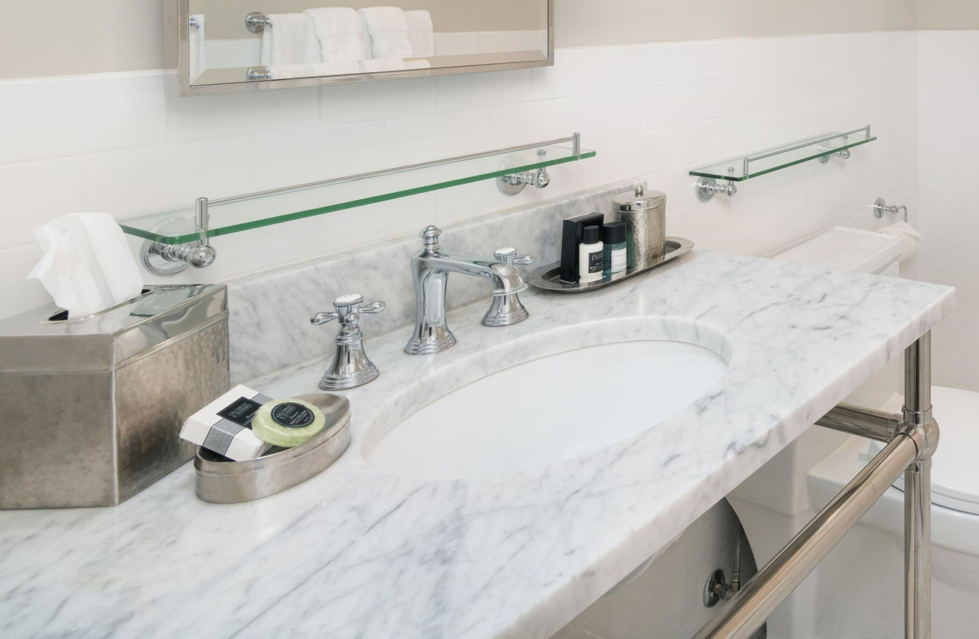 Een badkamer met een marmeren wastafel, chromen accessoires en glazen planken.