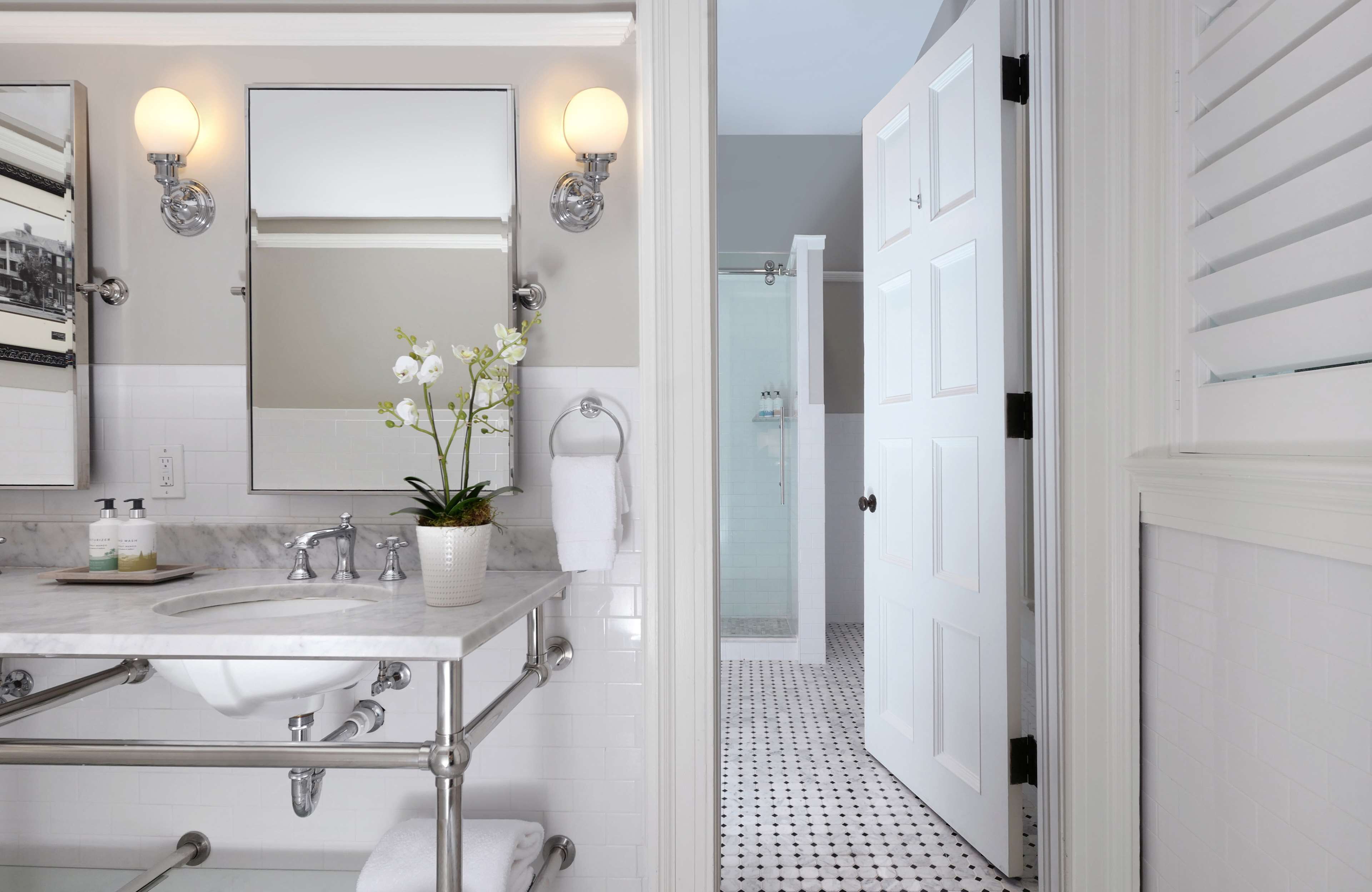 A modern bathroom with a marble sink, two wall-mounted lights, a potted orchid, and a glass shower enclosure.