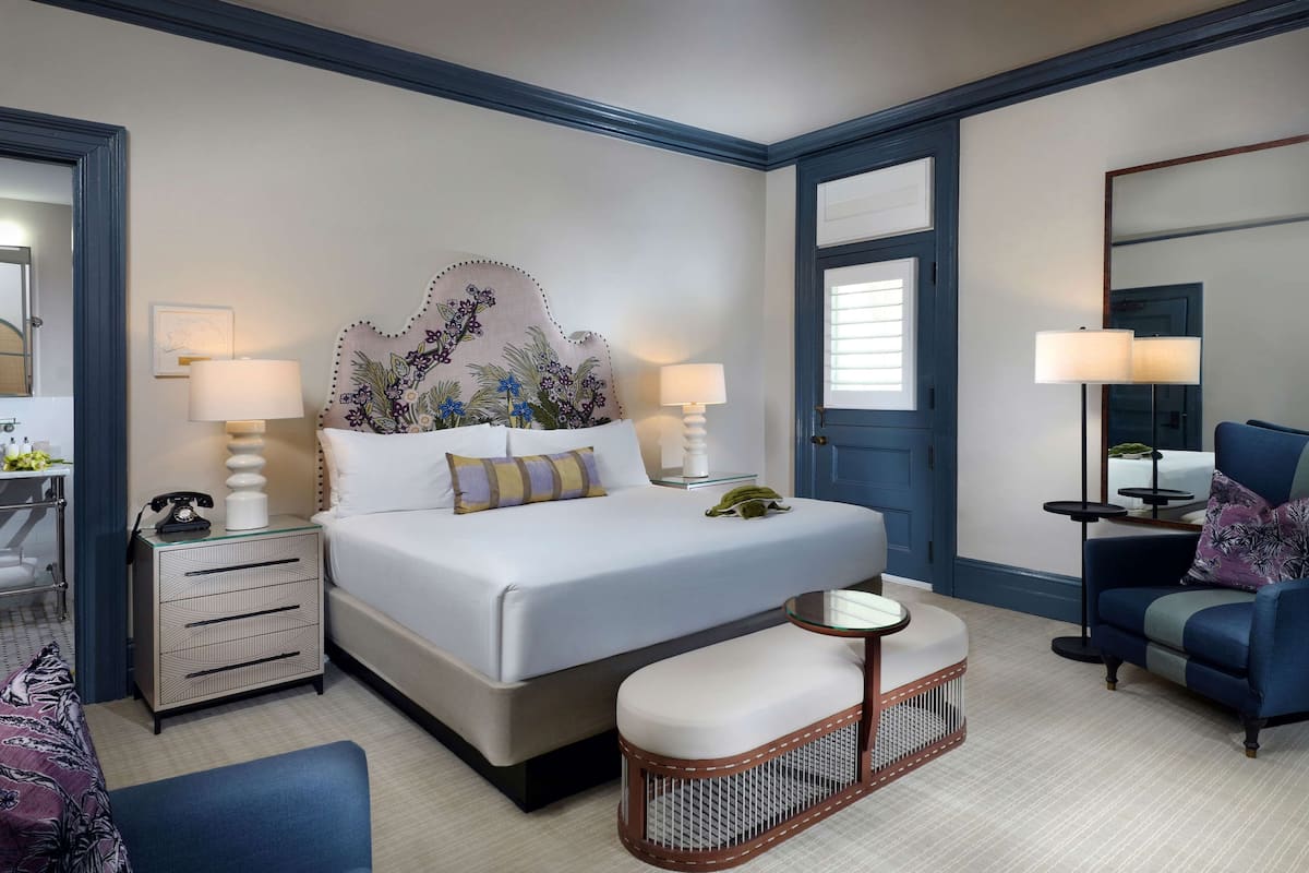 Une chambre d’hôtel avec un grand lit, des lampes de chevet, une chaise, une petite table et une tête de lit décorative.