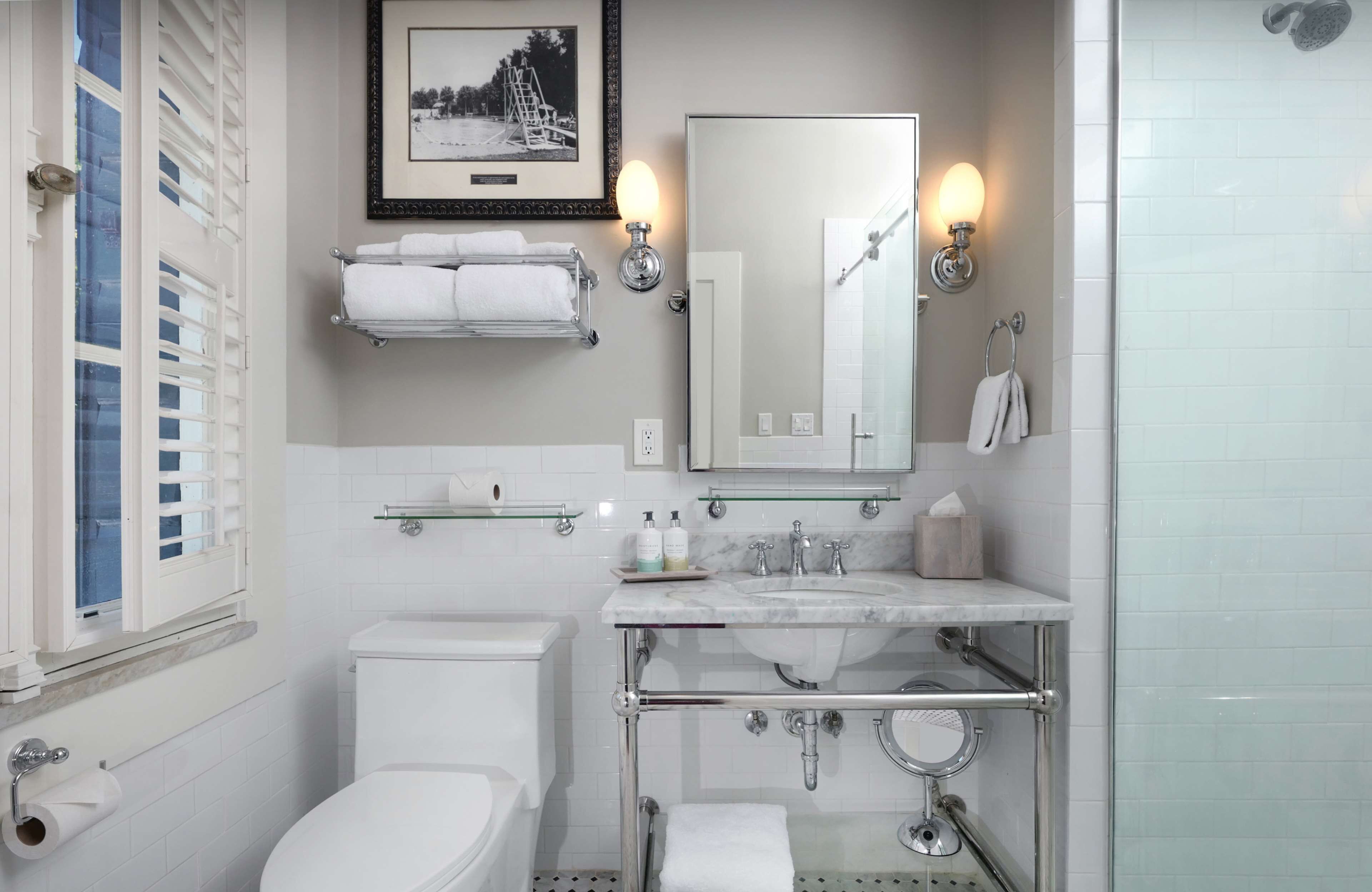 A modern bathroom with a toilet, sink, and shower. There are towels on a rack, a framed picture on the wall, and a glass shower enclosure.