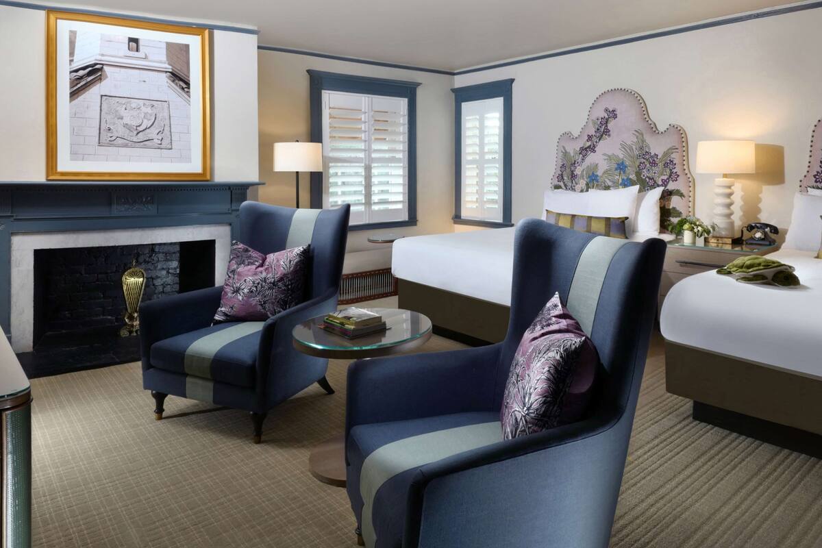 Une chambre d’hôtel avec une cheminée, deux fauteuils, un lit et une table de chevet avec des lampes.