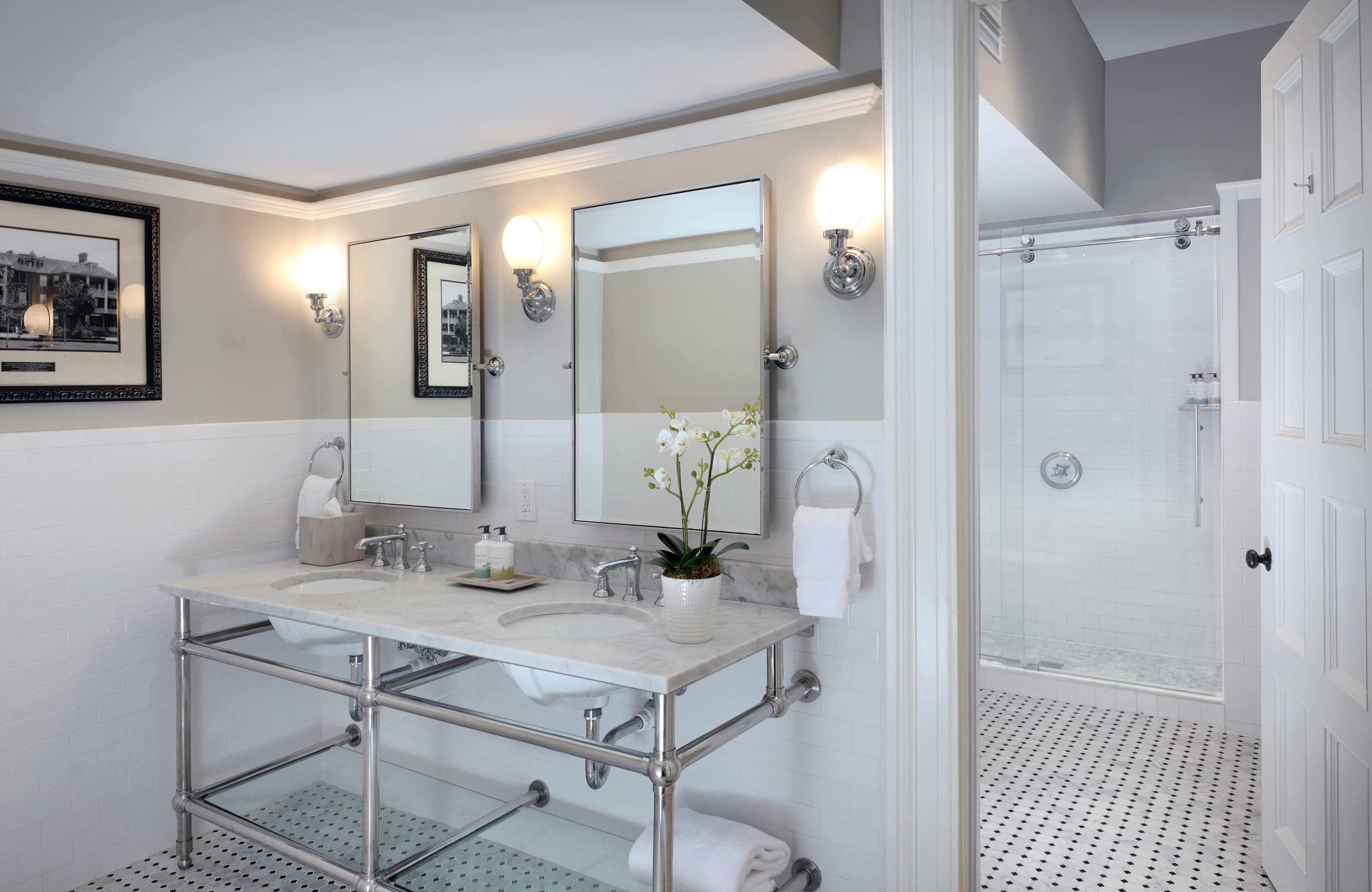 A modern bathroom with a double sink, a glass shower enclosure, and a large mirror with wall sconces.
