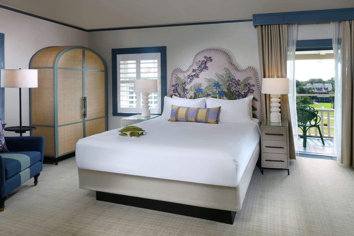 Une chambre d’hôtel avec un grand lit, un bureau avec une lampe, une chaise, une armoire et un balcon avec vue.