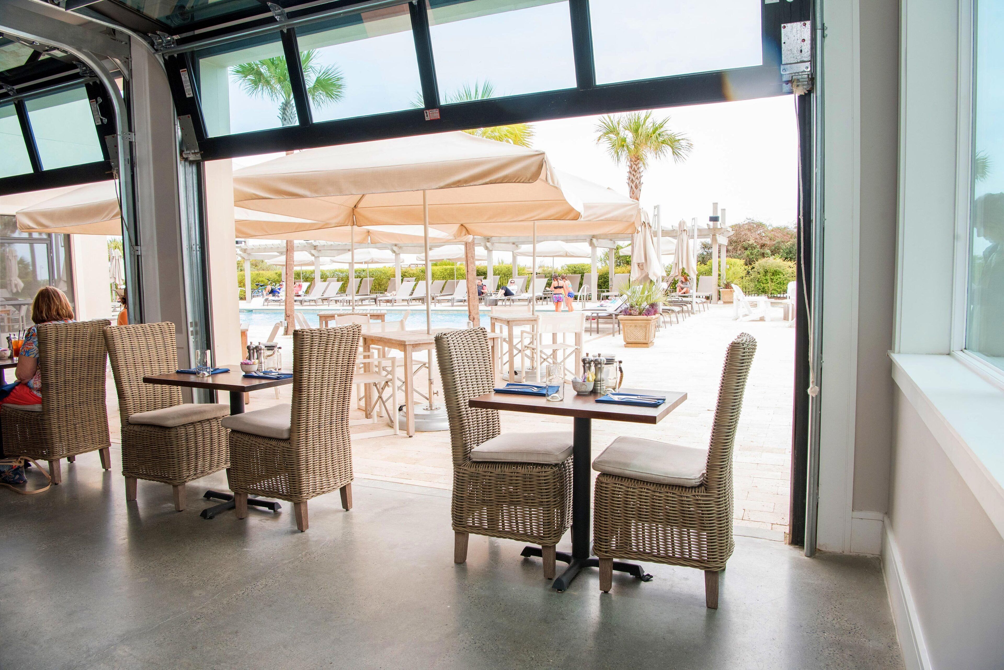 Un comedor interior con mobiliario de mimbre y vistas a una zona de piscina exterior.