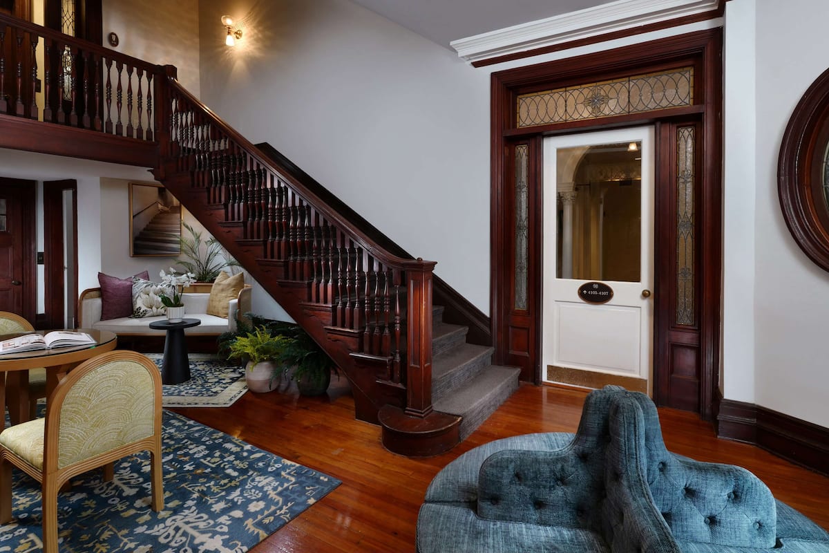 Un salon spacieux avec un escalier en bois, un fauteuil bleu, un canapé et un coin repas comprenant une table et des chaises.