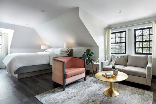 A modern hotel room with a bed, a chaise lounge, a sofa, a coffee table, and large windows.