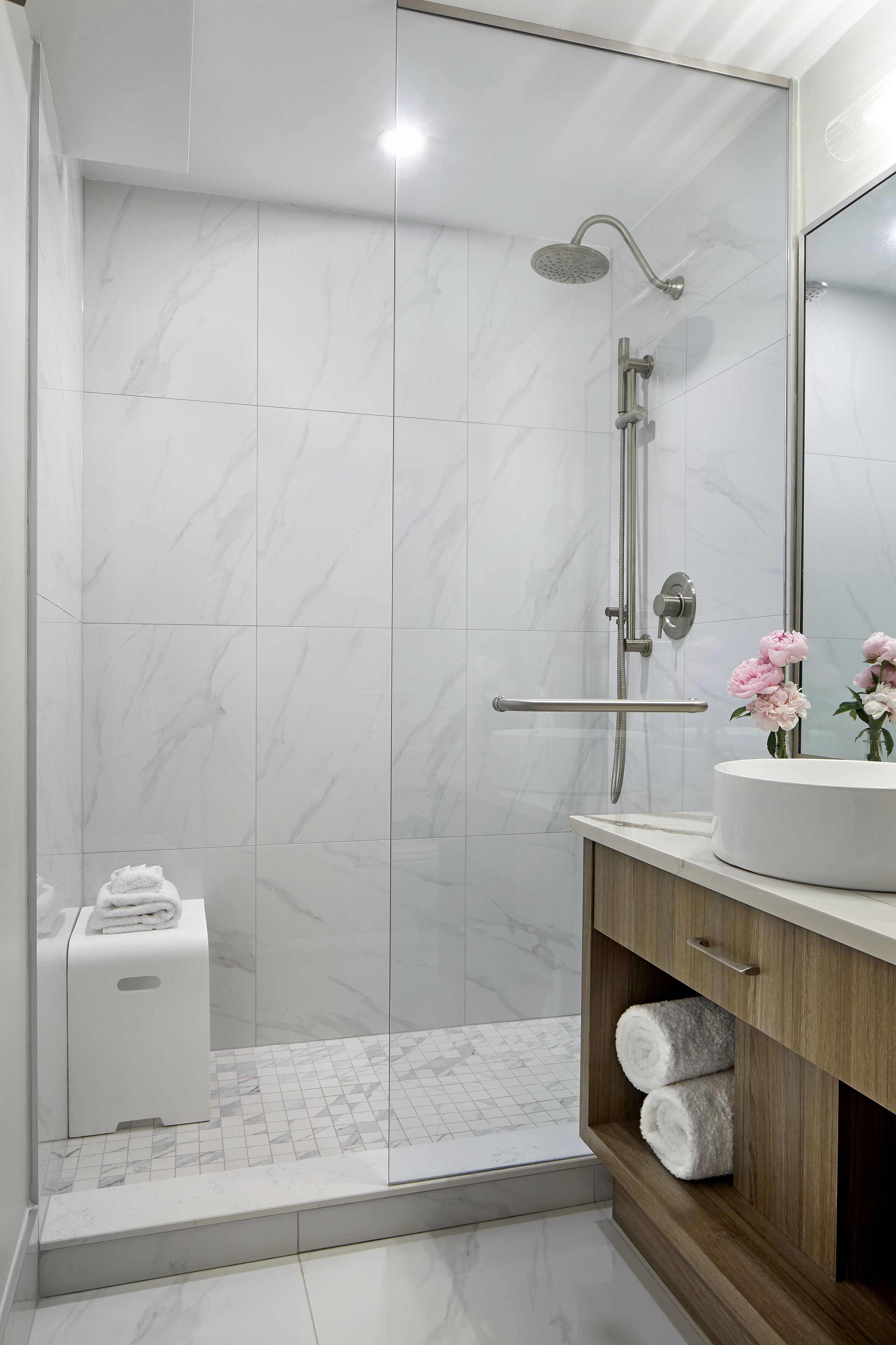 A modern bathroom with a glass shower enclosure, a wooden vanity, and a marble-tiled floor.