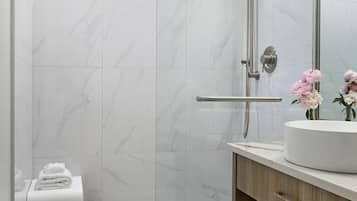 A modern bathroom with a glass shower enclosure, a wooden vanity, and a marble-tiled floor.