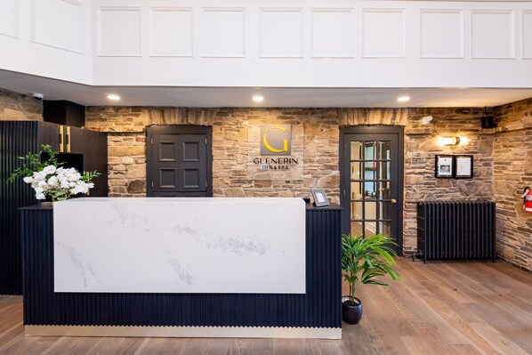 A reception desk with a marble top, flanked by dark wooden panels and a stone wall backdrop. A logo with a 'G' is displayed above the desk.