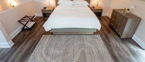 Ein ordentlich eingerichtetes Schlafzimmer mit einem großen Bett, Nachttischlampen, einem Holznachttisch, einer Kommode und einem gemusterten Teppich.