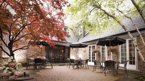 A patio area with brick flooring, outdoor seating, and hanging flower baskets.