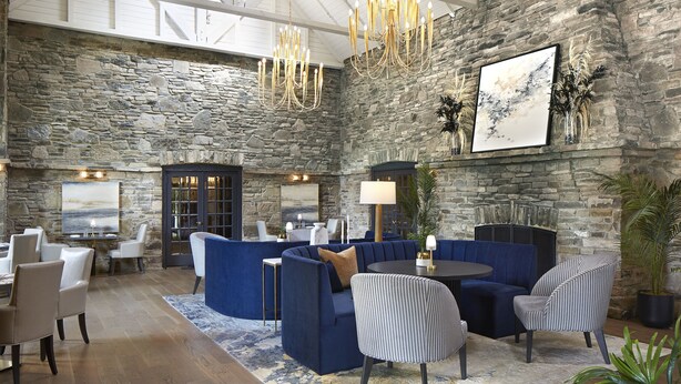 A spacious lobby with a stone wall, a chandelier, and seating arrangements including a blue sofa and chairs.