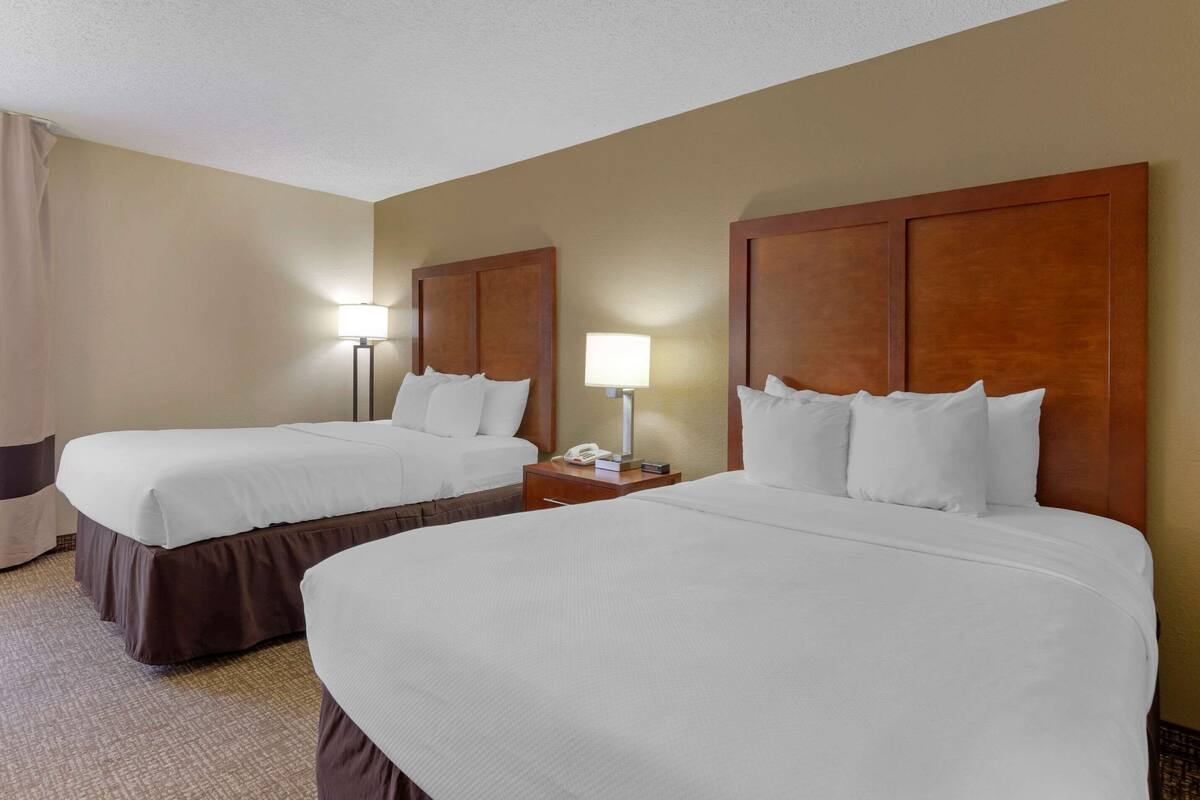 A hotel room with two beds, a nightstand with a lamp, and a telephone.