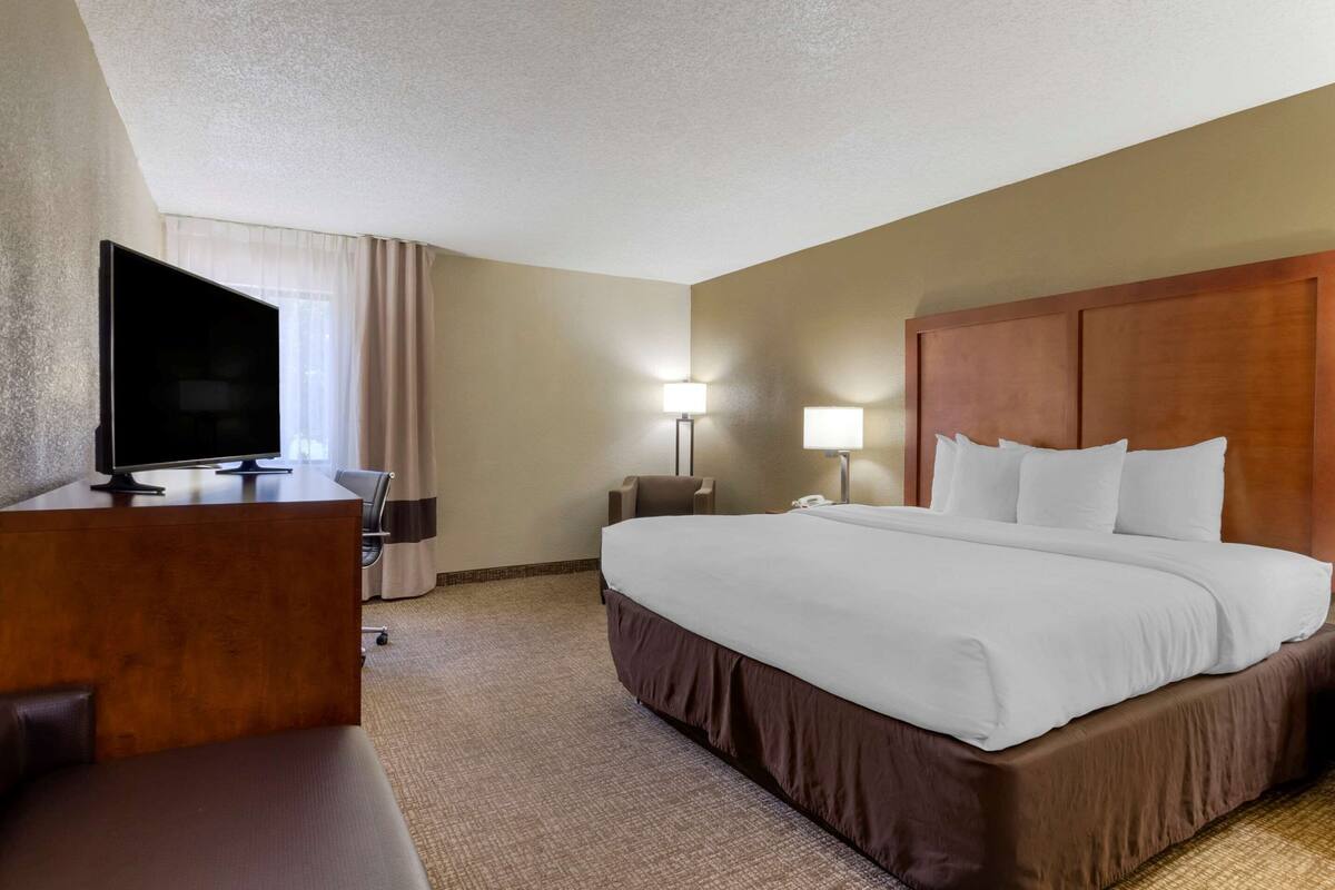 A hotel room with a large bed, a desk with a flat-screen TV, a lamp, and a nightstand.