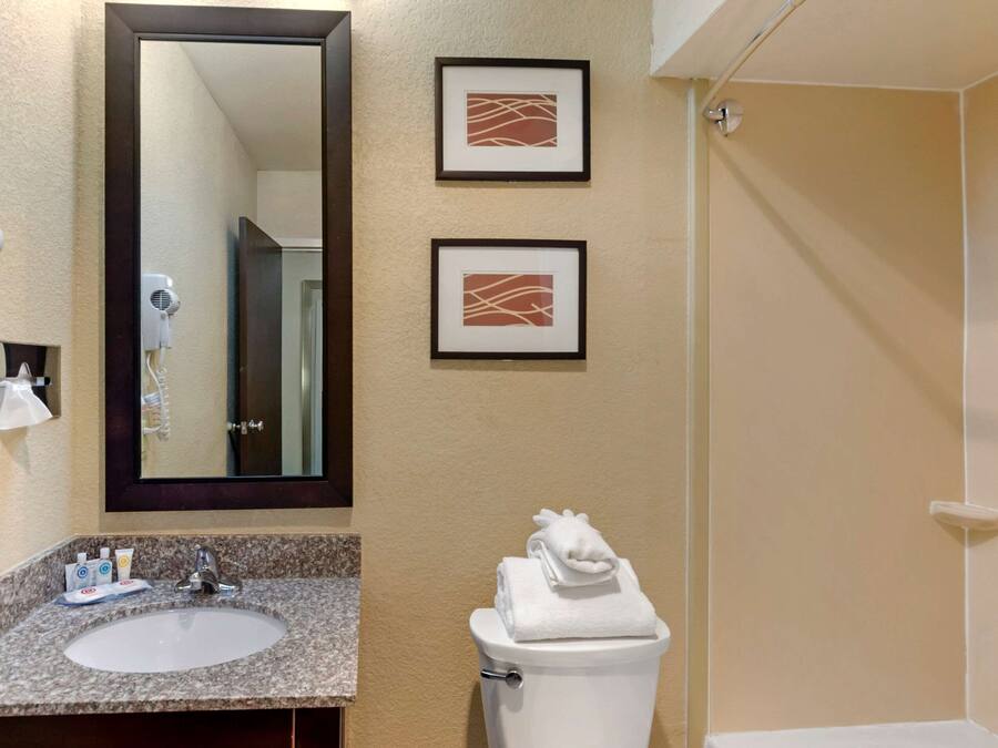 A bathroom with a sink, mirror, two framed pictures, a toilet, and a towel on the toilet.