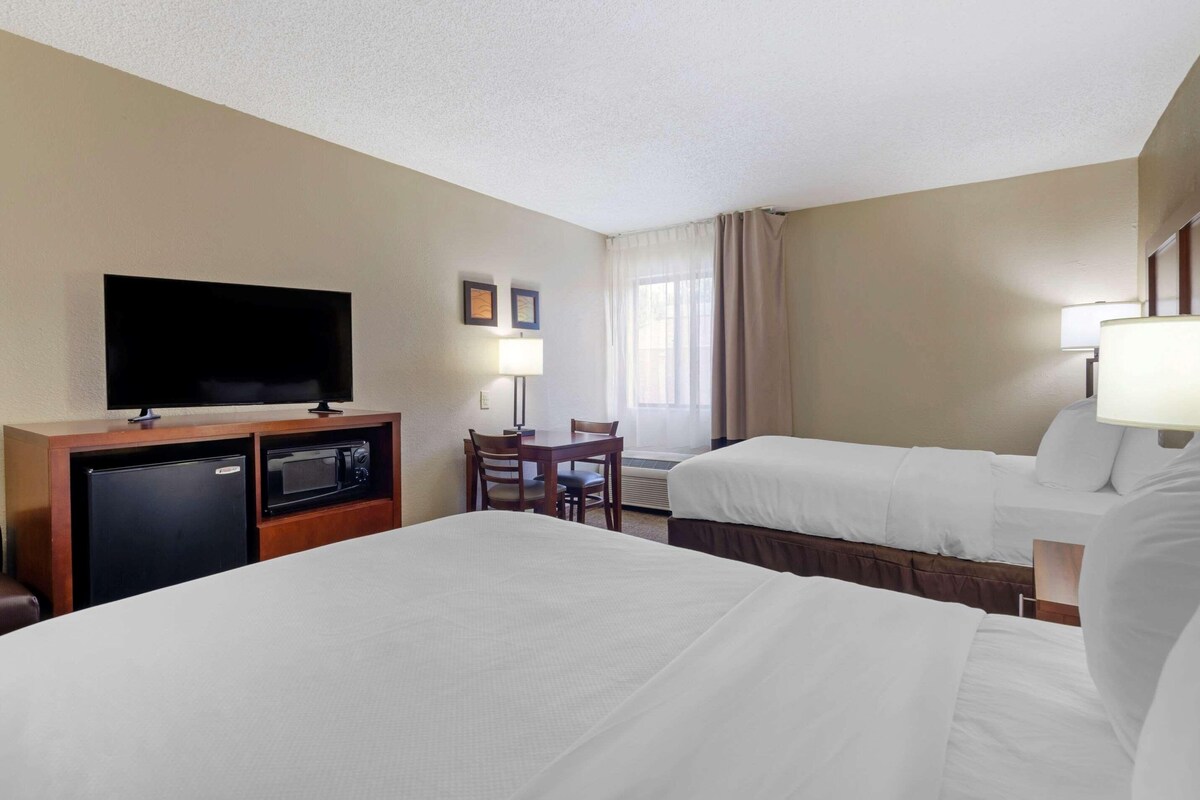 A hotel room with two beds, a desk with a television, a refrigerator, and a microwave.