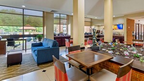 Un hall d’entrée spacieux, avec un canapé bleu, des tables et des chaises en bois. Une grande fenêtre offre une vue sur l’extérieur.