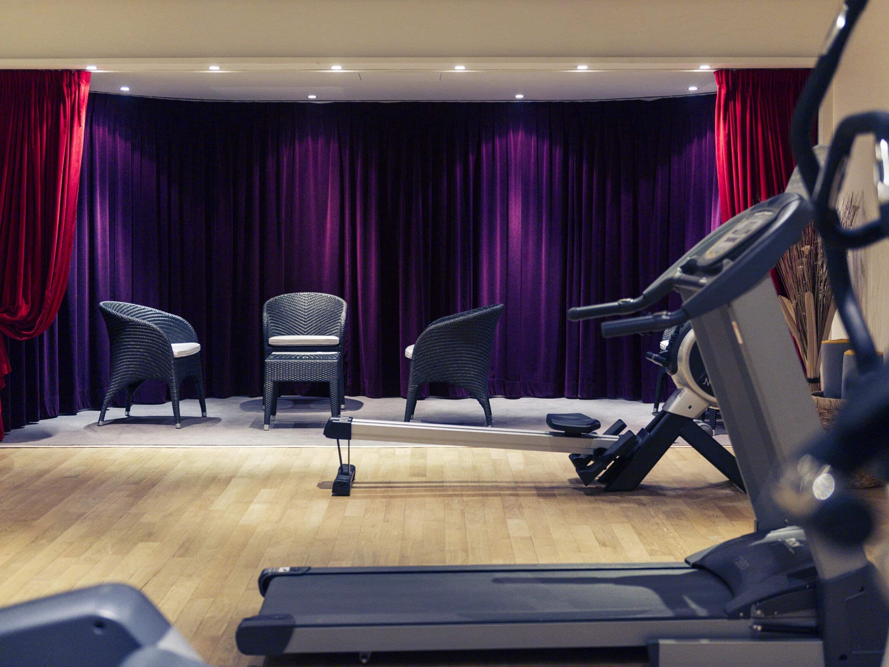 A room with a treadmill, two wicker chairs, and a stage with purple curtains.
