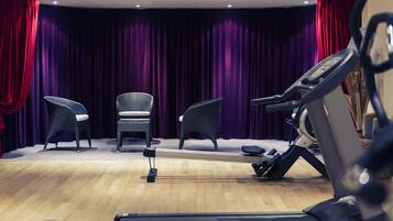 A room with a treadmill, two wicker chairs, and a stage with purple curtains.