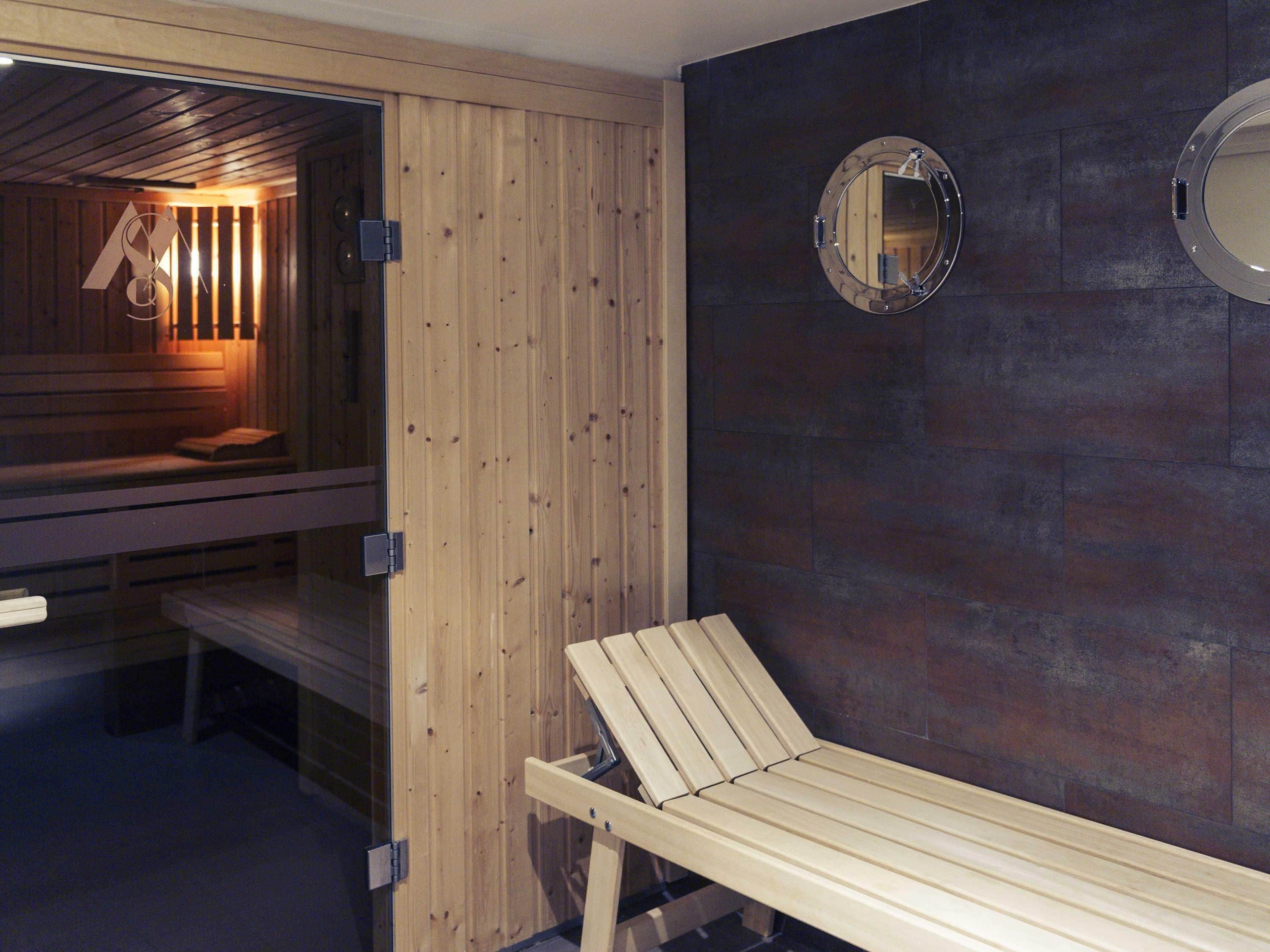 Un sauna avec des bancs en bois, un banc doté d’un dossier et un miroir fixé au mur.