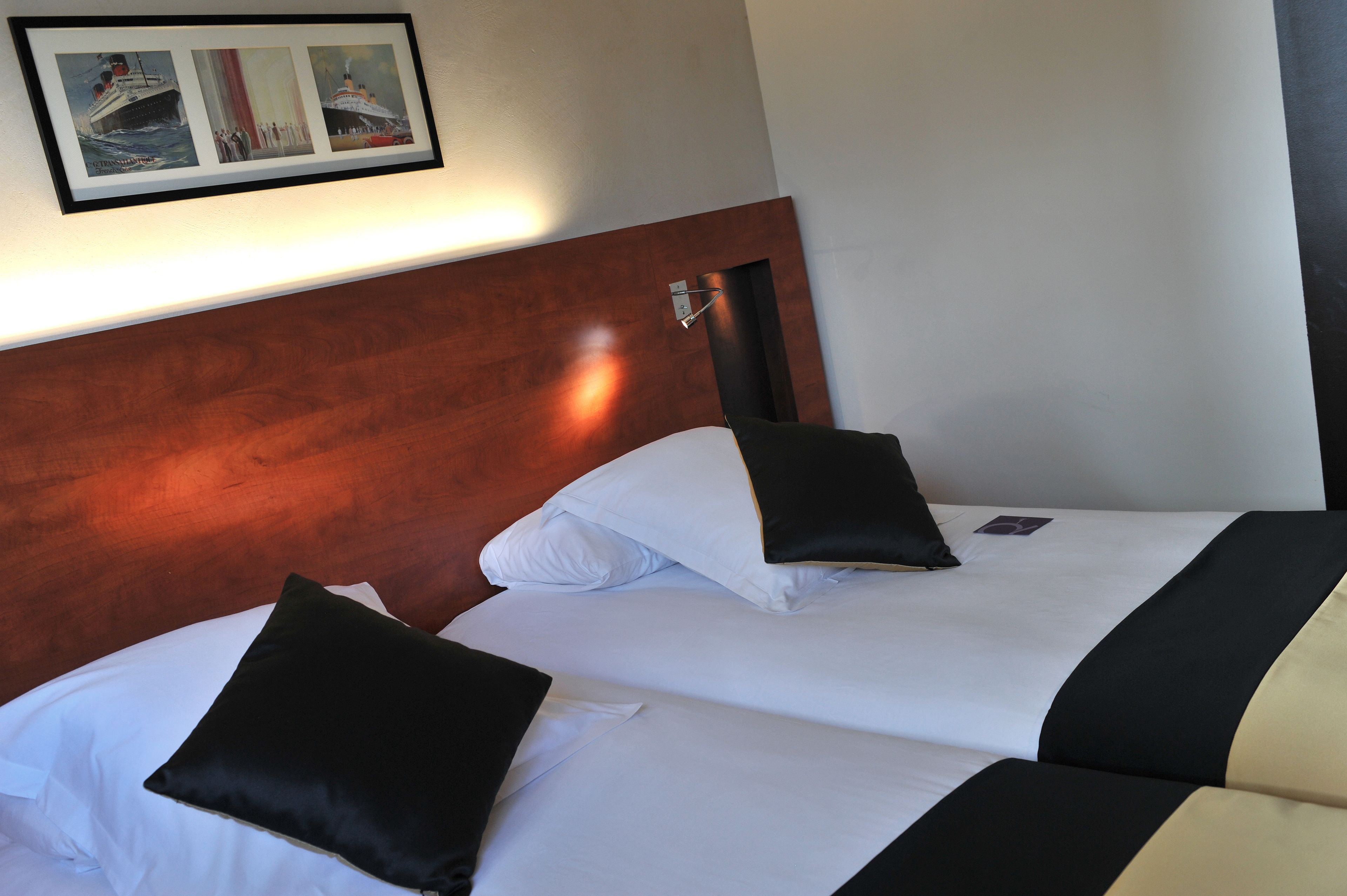 A hotel room with two beds, each with white linens and black and white pillows. There is a framed picture of a ship on the wall above the beds.