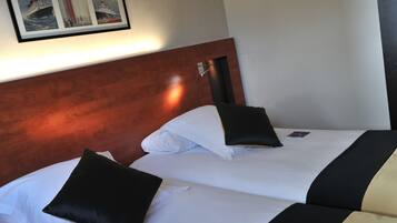 A hotel room with two beds, each with white linens and black and white pillows. There is a framed picture of a ship on the wall above the beds.
