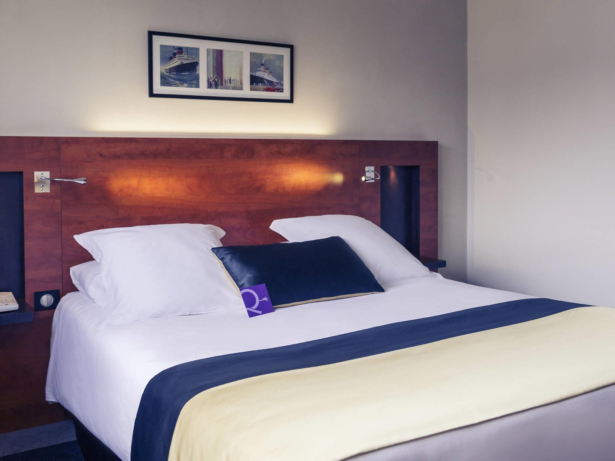 A hotel room with a wooden headboard, a bed with white and blue bedding, and a framed picture above the bed.
