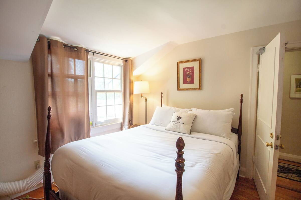 A neatly made bed with white linens, a bedside lamp, and a framed picture on the wall.