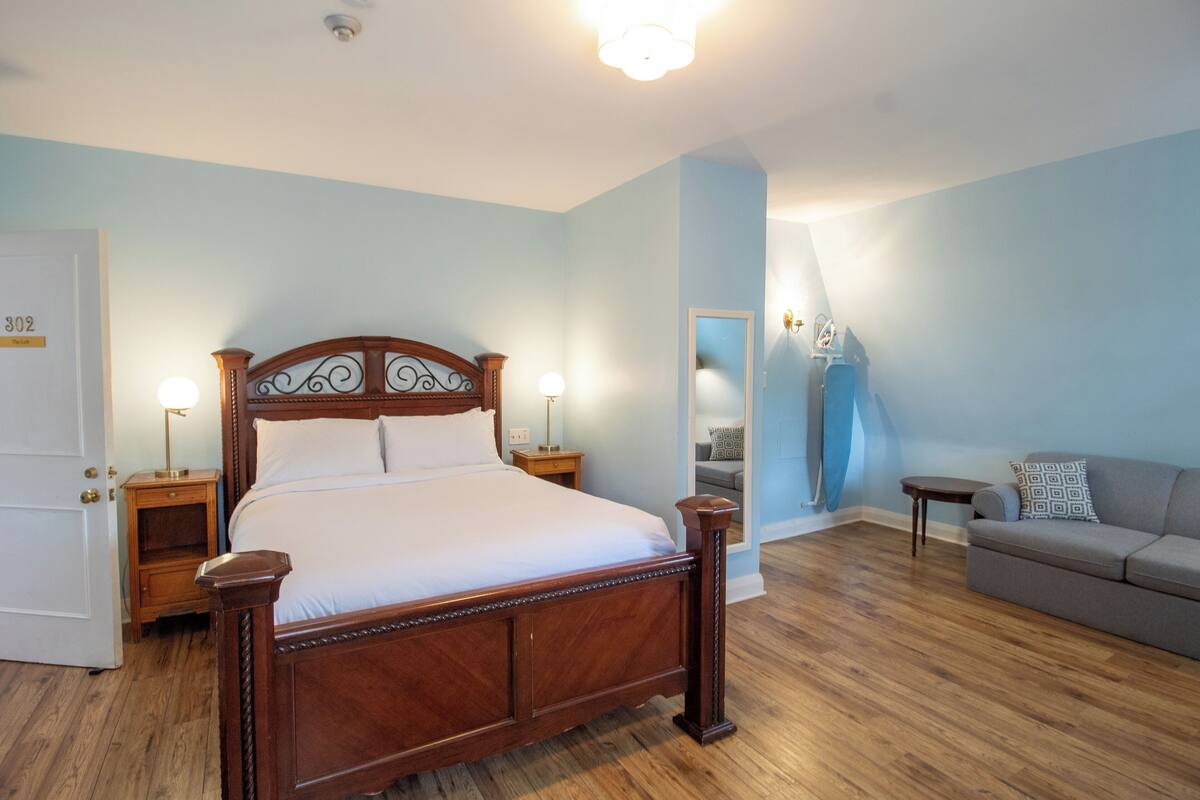 A bedroom with a wooden bed, a nightstand, a bedside table, a sofa, and a mirror.