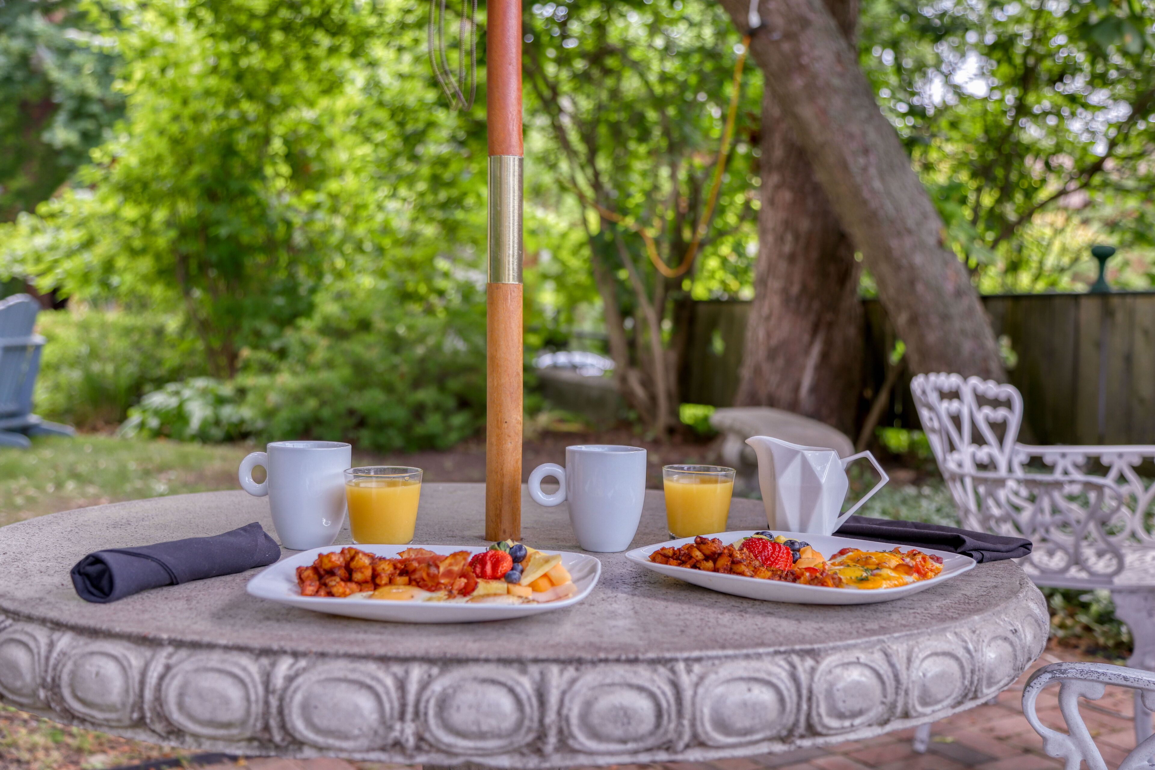 A round table with two plates of food, two cups of orange juice, and a pitcher of orange juice.