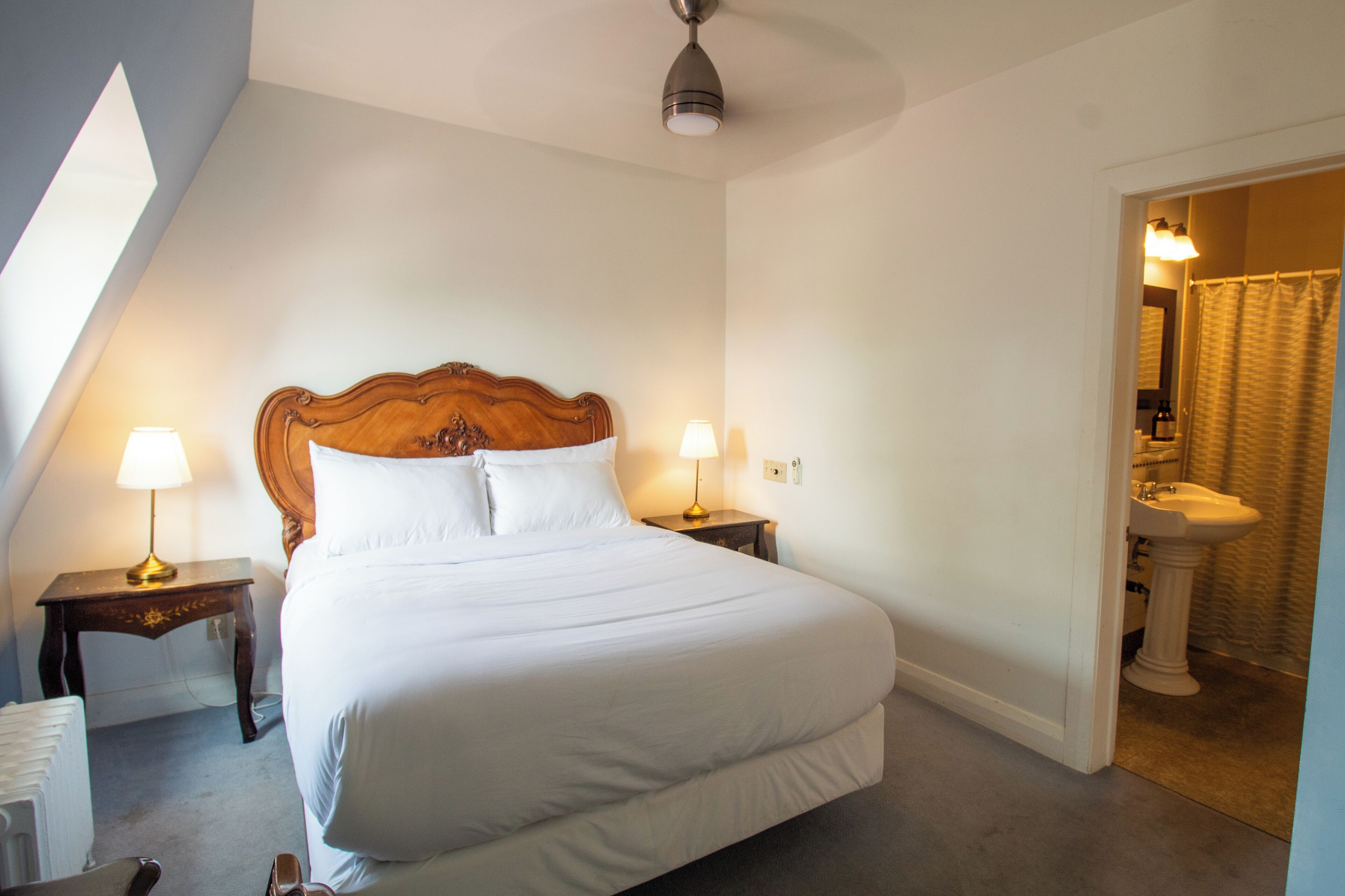 A neatly made bed with white linens, two bedside lamps, and a wooden headboard.