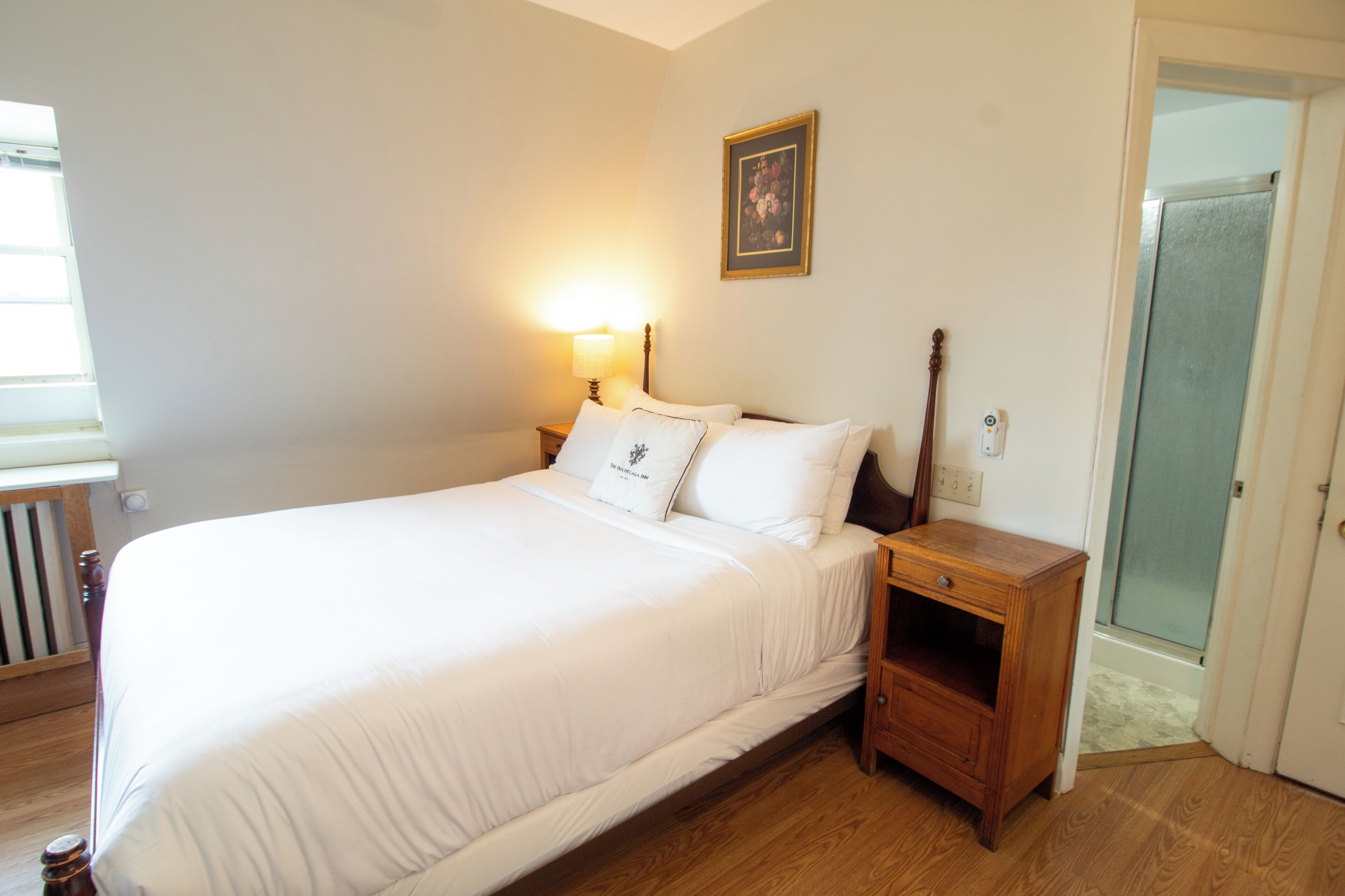 A bedroom with a bed, bedside table, lamp, and a door leading to a bathroom.