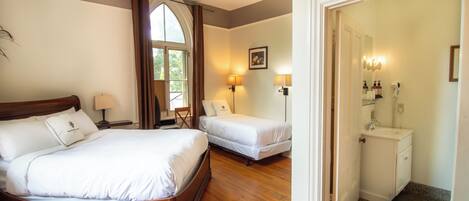 A hotel room with a large bed, two smaller beds, a bathroom with a sink and mirror, and a ceiling fan.