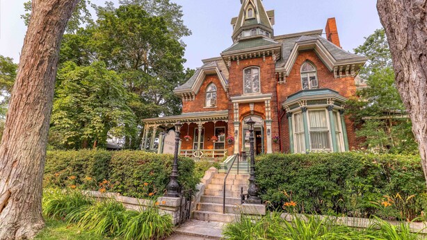 Une grande maison historique en briques, dotée d’une tour imposante, entourée d’une végétation luxuriante et d’un jardin bien entretenu.