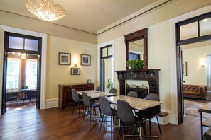 A dining area with a marble table, chairs, and a fireplace. There is a sofa and a plant in the adjacent living room.