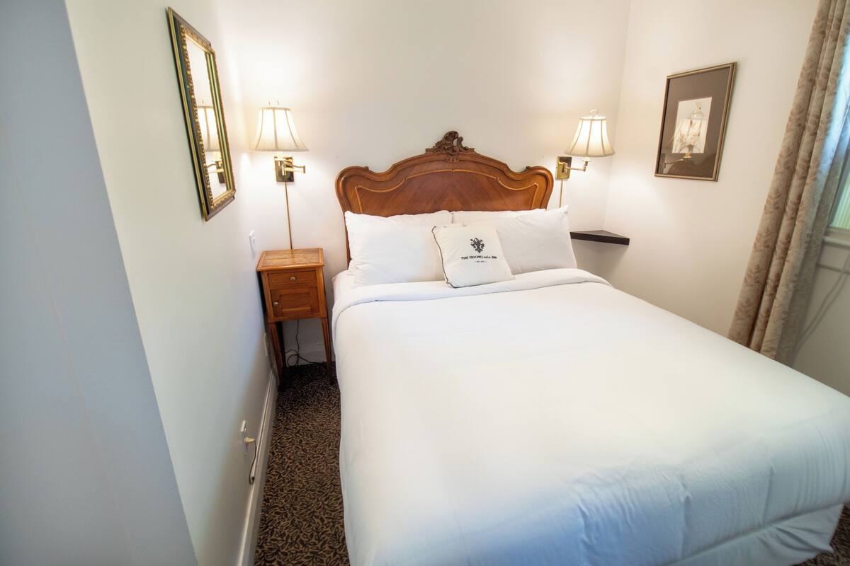 A neatly made bed with a wooden headboard, two bedside lamps, and a framed picture on the wall.