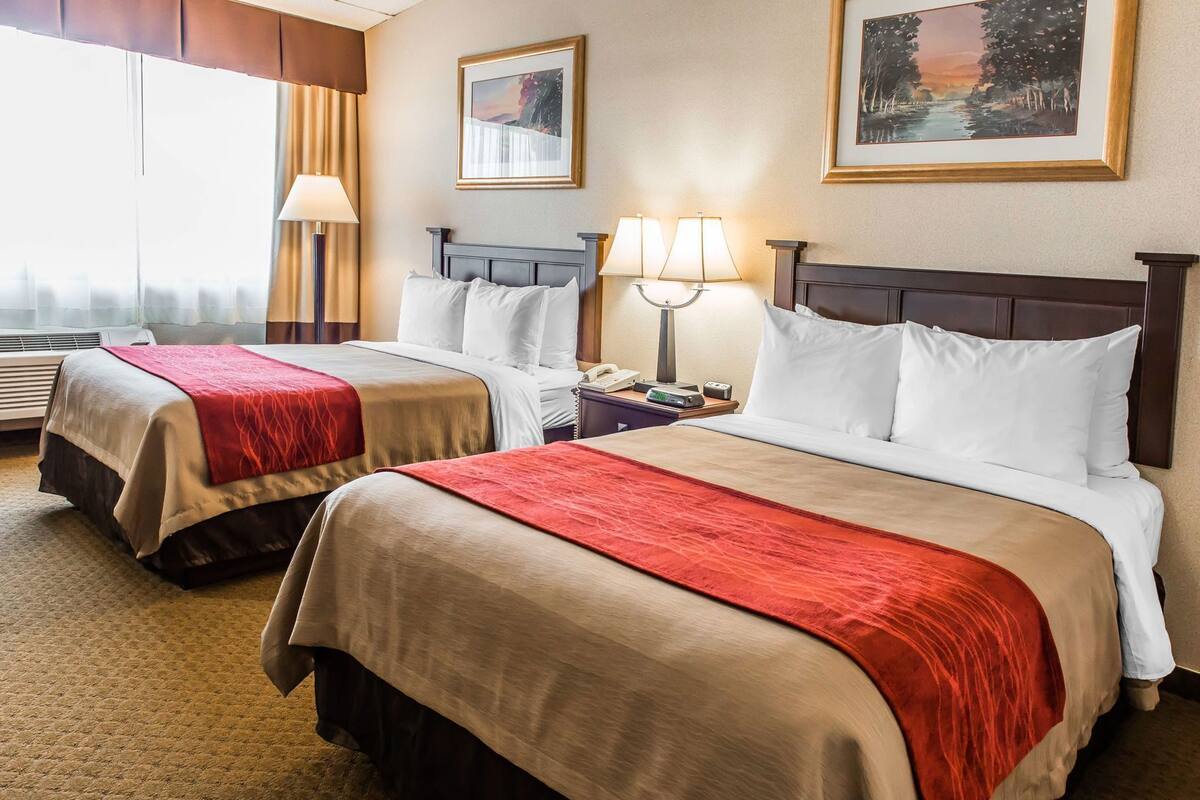 A hotel room with two beds, a nightstand with a lamp, a phone, and a clock.