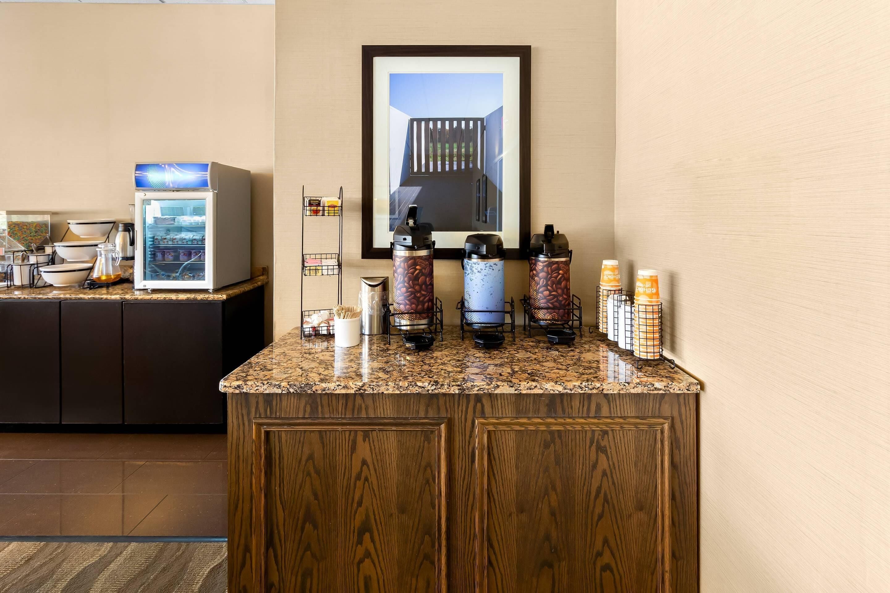 A kitchen area with a coffee machine, a refrigerator, and a coffee dispenser on a granite countertop.