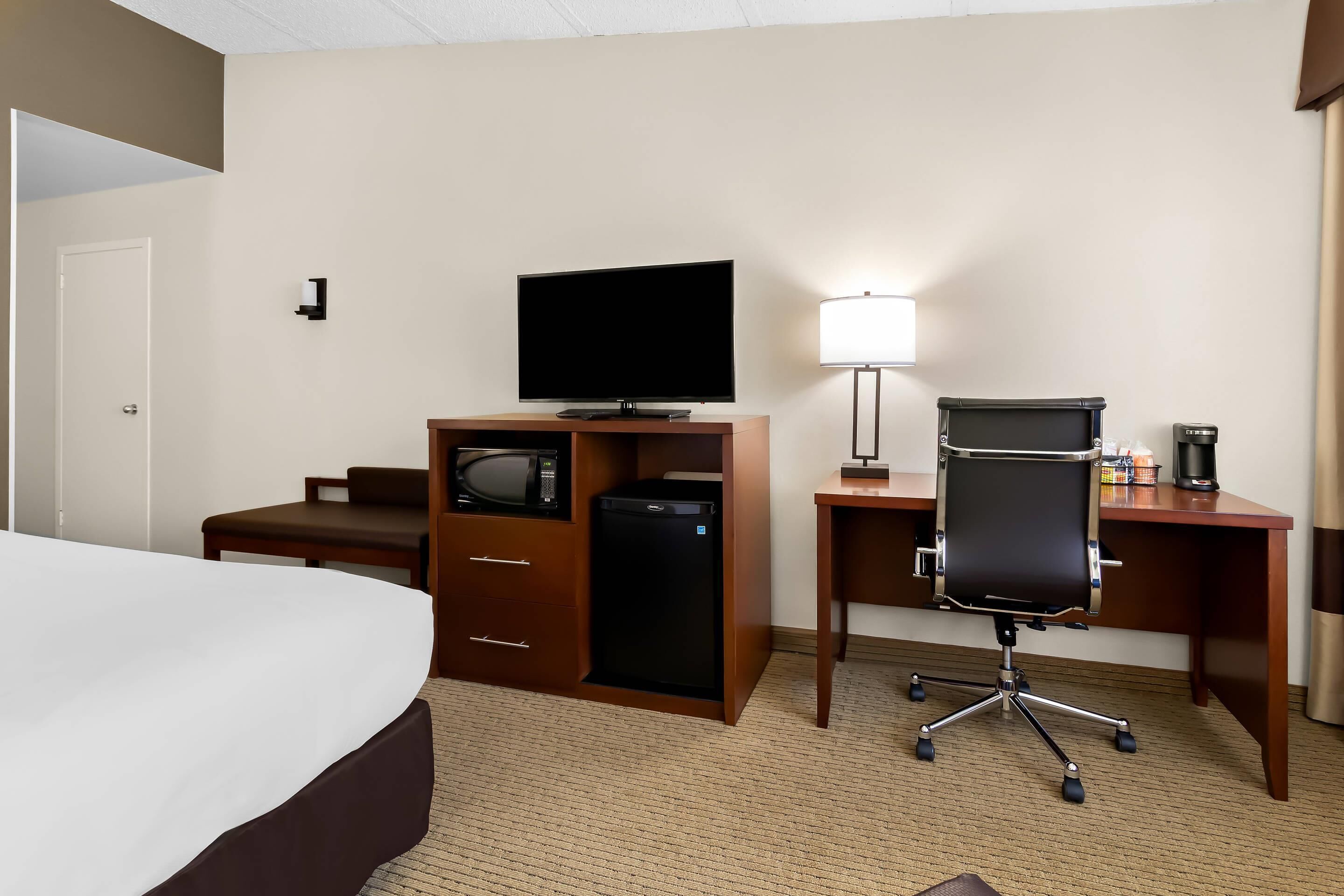 Hotelkamer met een bed, televisie, bureau met stoel, lamp, koffiezetapparaat en minibar.