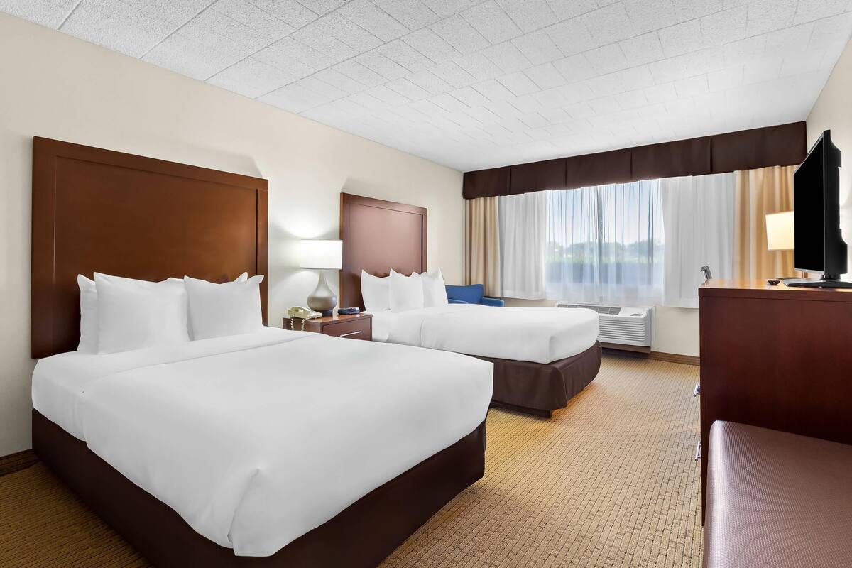 A hotel room with two beds, a desk, a chair, a TV, and a window with curtains.