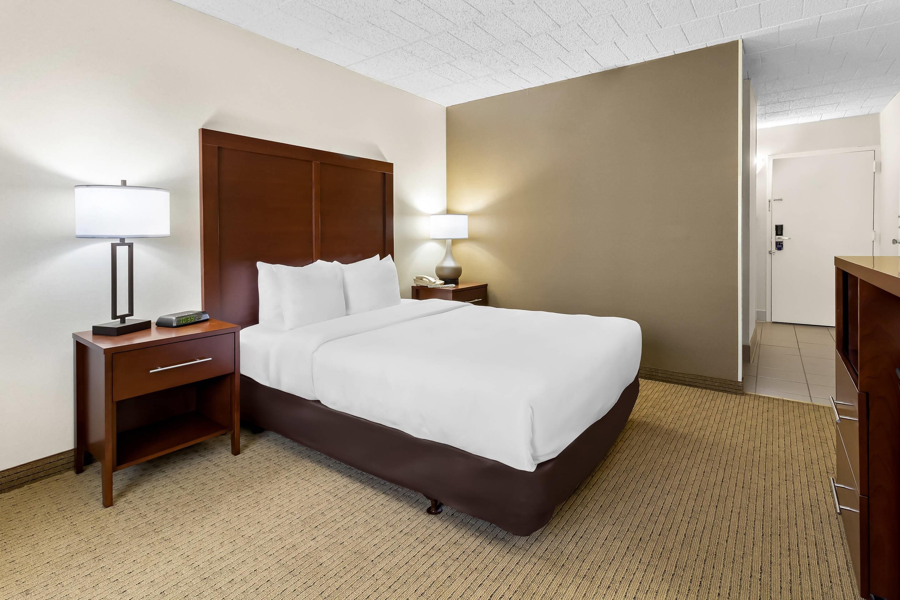 Una habitación de hotel con cama, mesitas de noche, lámparas y una puerta.