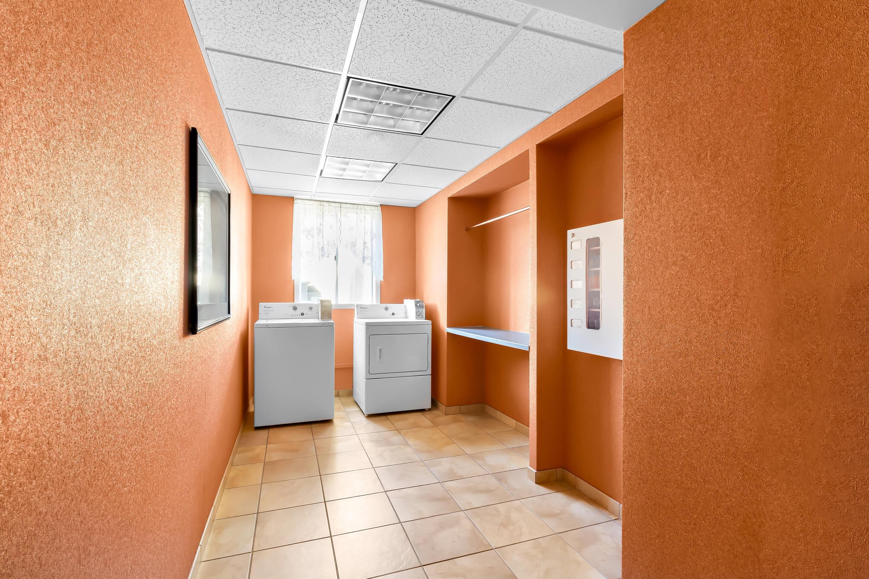 A narrow hallway with orange walls, a tiled floor, and two white laundry machines.
